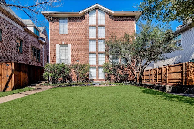 rear view of property with a lawn, fence, and brick siding