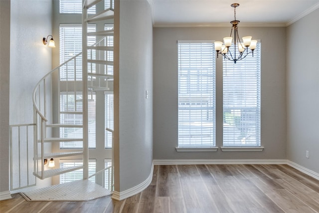entryway with wood finished floors, crown molding, and a notable chandelier