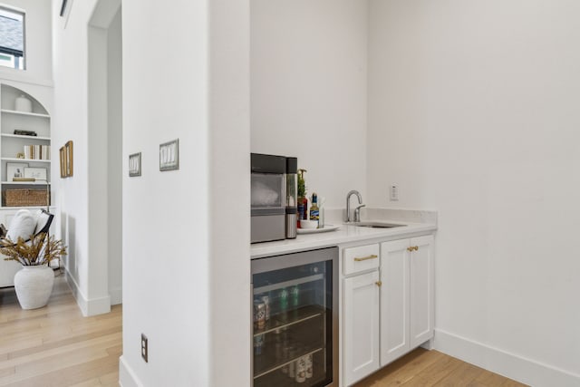 bar featuring light wood-style floors, baseboards, a sink, and wine cooler