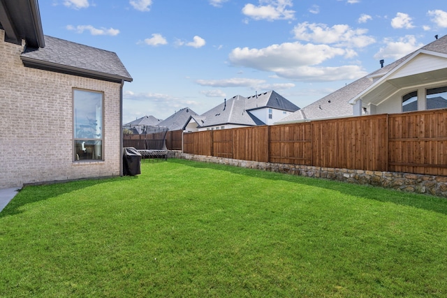 view of yard featuring a trampoline, a fenced backyard, and a residential view
