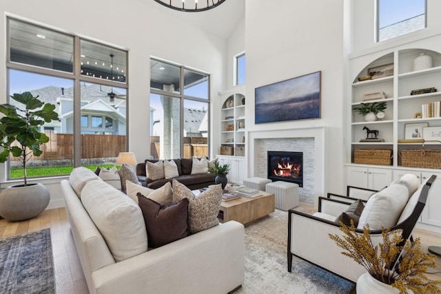 living area with light wood-type flooring, a towering ceiling, a glass covered fireplace, and built in shelves