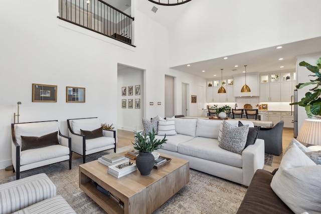 living room featuring a high ceiling, light wood-style flooring, visible vents, and recessed lighting