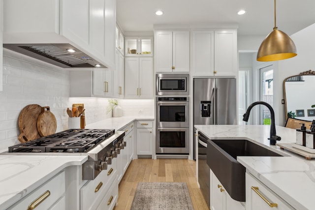 kitchen with decorative backsplash, stainless steel appliances, white cabinets, a sink, and light wood-type flooring