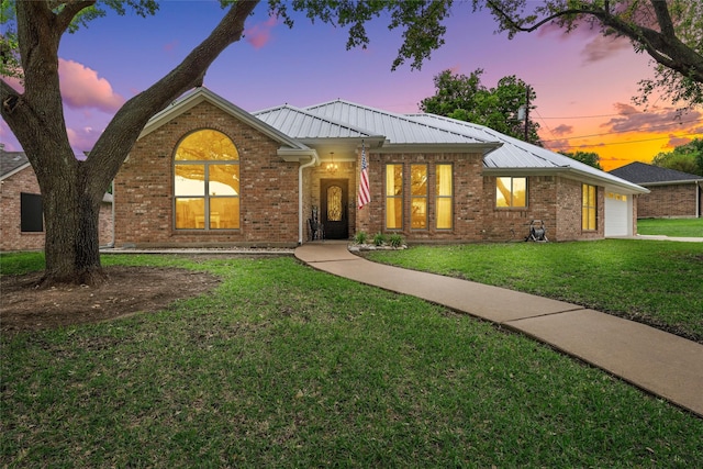 ranch-style house with metal roof, a yard, an attached garage, and brick siding