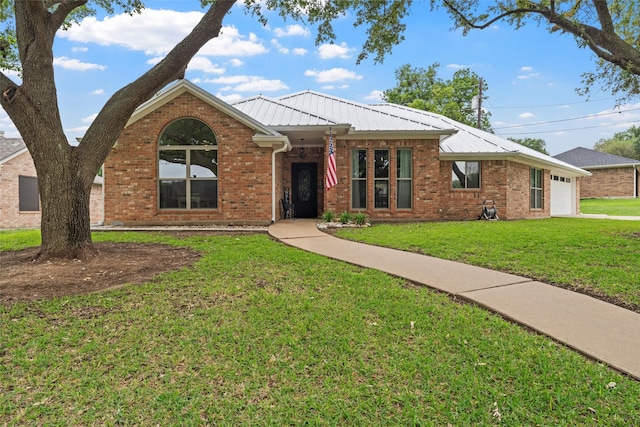 single story home featuring metal roof, a front yard, a garage, and brick siding