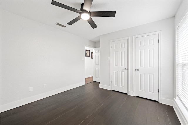 unfurnished bedroom with dark wood-type flooring, visible vents, a ceiling fan, and baseboards
