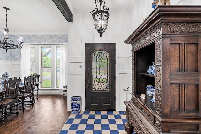 foyer entrance with crown molding, a chandelier, a decorative wall, wood finished floors, and wainscoting