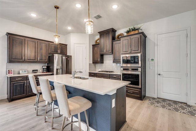 kitchen with appliances with stainless steel finishes, dark brown cabinets, light countertops, and a sink