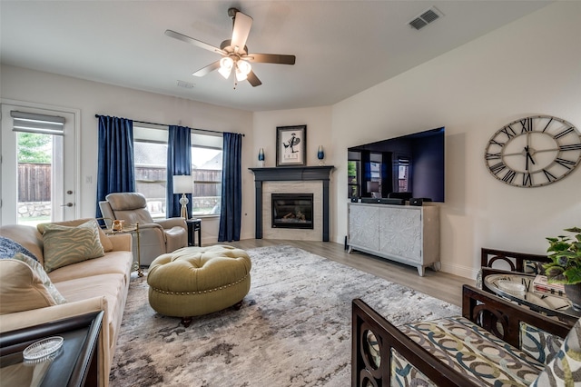 living area featuring a glass covered fireplace, visible vents, ceiling fan, and wood finished floors