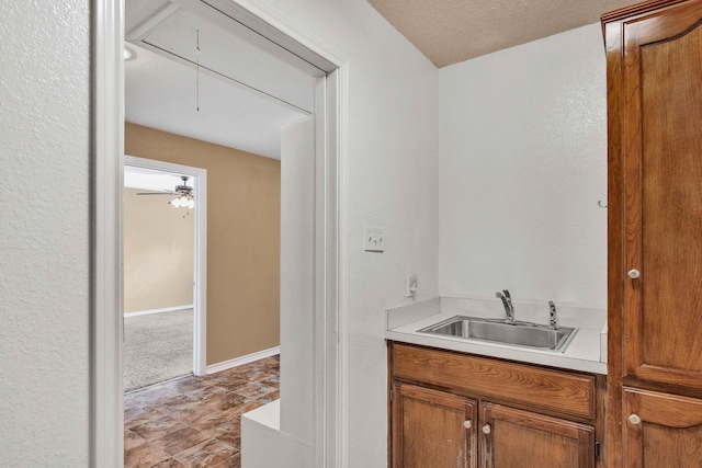 bar featuring a textured wall, baseboards, and a sink