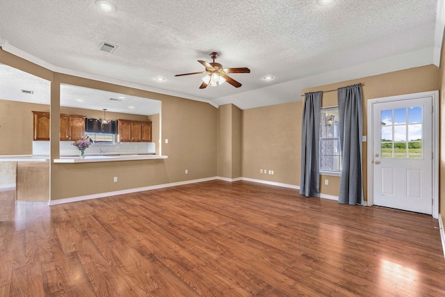 unfurnished living room with wood finished floors, a ceiling fan, a textured ceiling, and ornamental molding