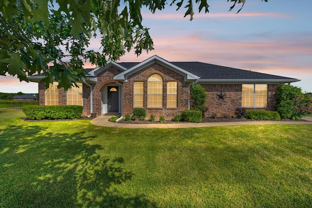 ranch-style house featuring brick siding, a front lawn, and roof with shingles
