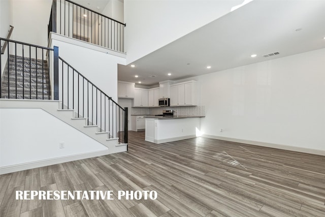 unfurnished living room featuring light wood-style flooring, visible vents, recessed lighting, a towering ceiling, and stairs