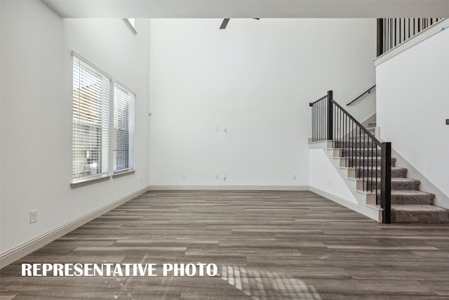 unfurnished living room featuring baseboards, stairway, and wood finished floors
