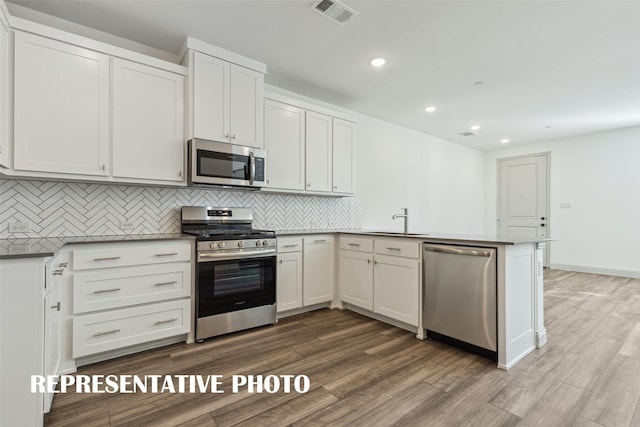 kitchen with a sink, visible vents, stainless steel appliances, dark wood finished floors, and a peninsula