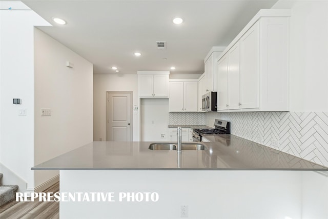 kitchen with stainless steel appliances, backsplash, a sink, visible vents, and a peninsula