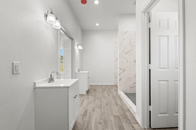 full bath with recessed lighting, wood finished floors, two vanities, a sink, and a marble finish shower