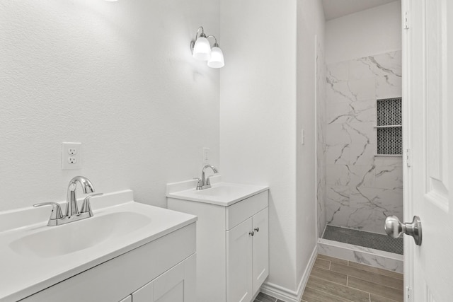 full bath with two vanities, wood finish floors, a marble finish shower, and a sink