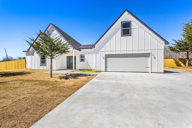 modern farmhouse featuring driveway, board and batten siding, an attached garage, fence, and a front lawn