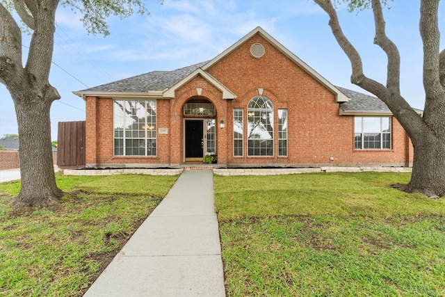 view of front of house with brick siding, a shingled roof, and a front lawn