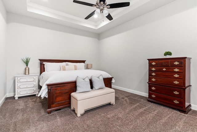 bedroom with baseboards, ceiling fan, dark carpet, and a raised ceiling