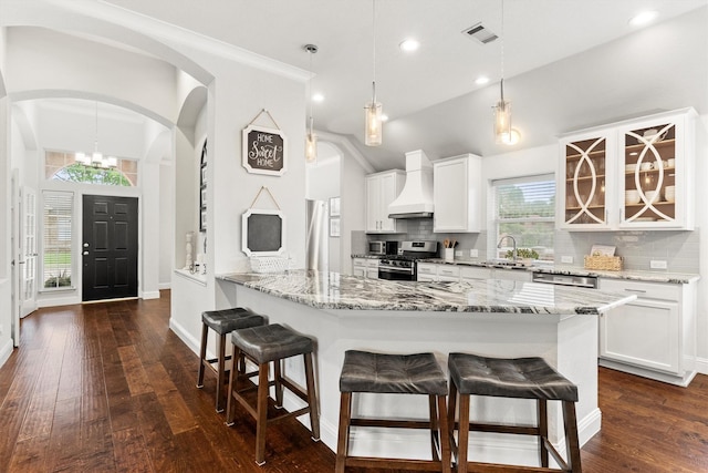 kitchen featuring custom exhaust hood, a kitchen breakfast bar, appliances with stainless steel finishes, backsplash, and vaulted ceiling