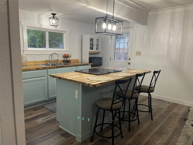 kitchen with a sink, wood counters, dark wood-style flooring, a kitchen breakfast bar, and black appliances