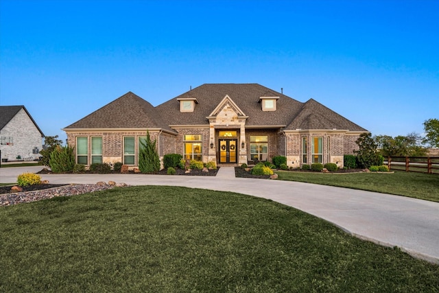 french country home featuring brick siding, fence, curved driveway, french doors, and a front yard