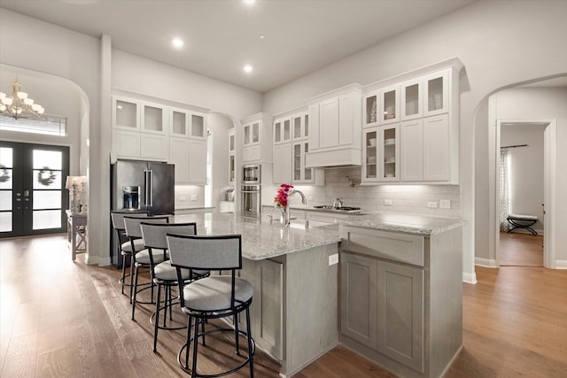 kitchen featuring white cabinets, arched walkways, appliances with stainless steel finishes, and light wood-style flooring