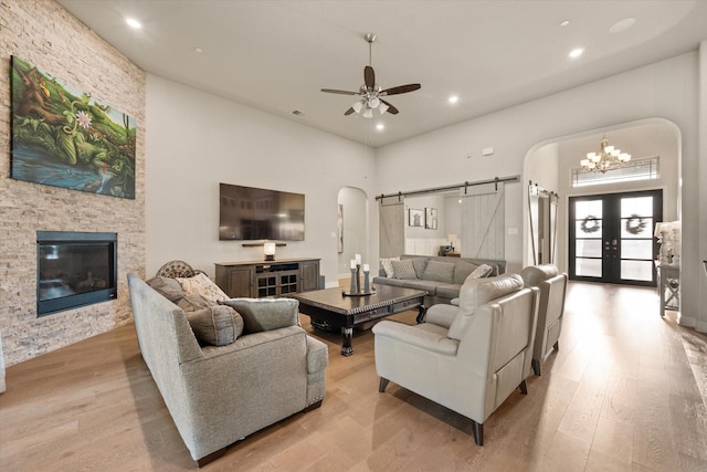 living area with light wood finished floors, recessed lighting, a barn door, arched walkways, and ceiling fan with notable chandelier