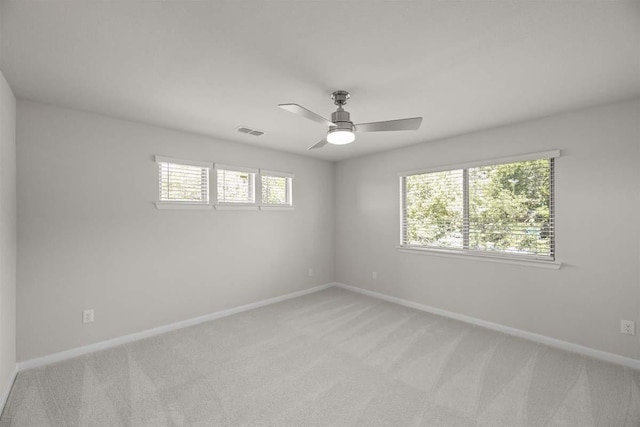 empty room with a ceiling fan, visible vents, light colored carpet, and baseboards