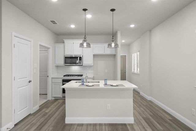 kitchen with visible vents, stainless steel microwave, white cabinets, a sink, and light wood-type flooring