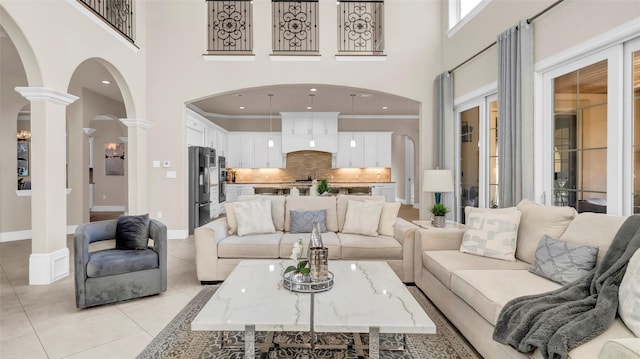 living room with arched walkways, decorative columns, light tile patterned floors, crown molding, and a towering ceiling