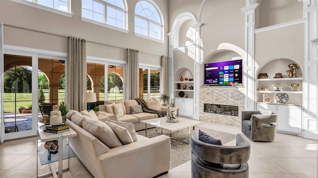 living room with light tile patterned floors, built in shelves, a stone fireplace, and a towering ceiling