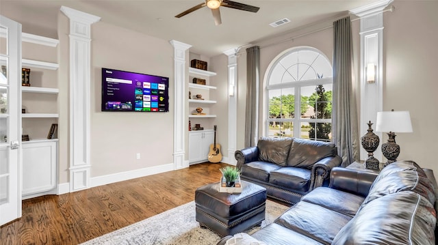 living room featuring ceiling fan, decorative columns, built in features, visible vents, and wood finished floors
