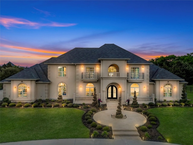 french provincial home with a lawn, stucco siding, french doors, and a balcony