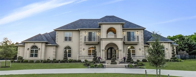french country home featuring a high end roof, a balcony, a front yard, and stucco siding