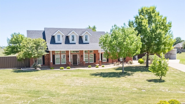 cape cod house featuring a front yard, fence, a shingled roof, and brick siding
