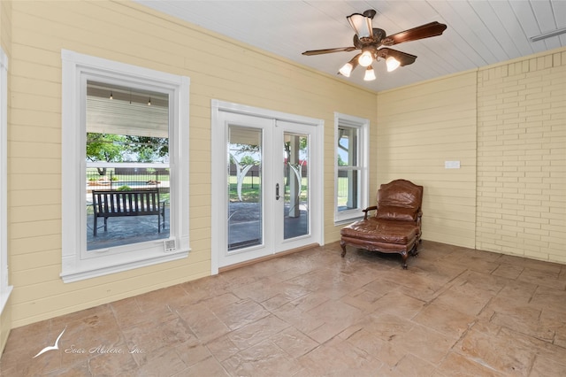 sitting room with visible vents, wood walls, a ceiling fan, and french doors