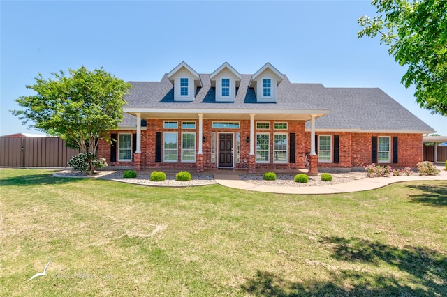new england style home featuring fence, a front lawn, a shingled roof, and brick siding