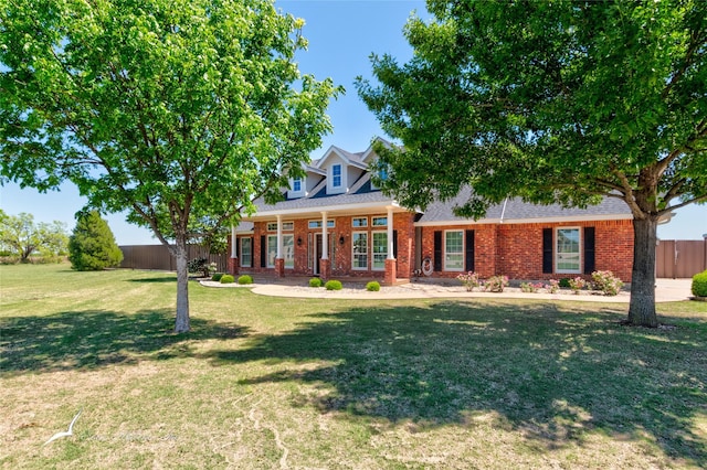 view of front of property with fence, a front yard, a shingled roof, and brick siding