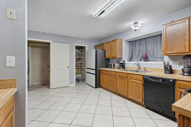 kitchen with freestanding refrigerator, dishwasher, a sink, a textured ceiling, and light tile patterned flooring