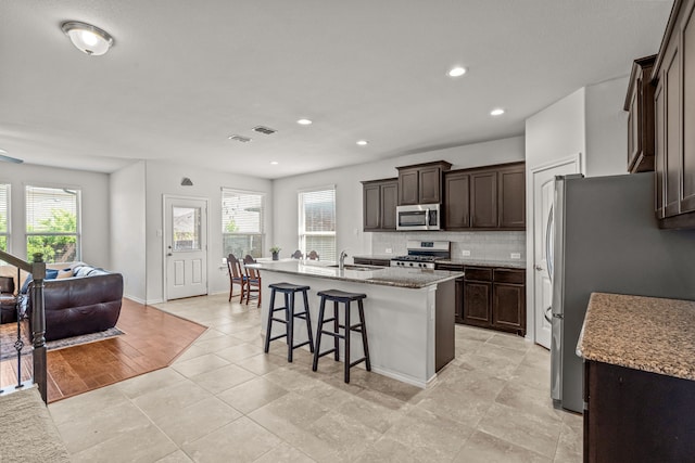 kitchen with tasteful backsplash, a sink, appliances with stainless steel finishes, dark brown cabinets, and a kitchen bar