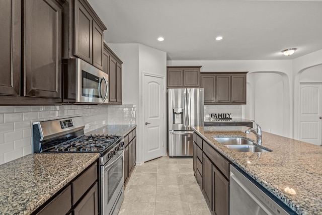 kitchen with stone counters, a sink, dark brown cabinets, and stainless steel appliances