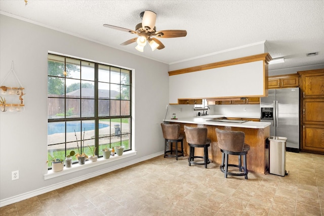 kitchen featuring stainless steel fridge with ice dispenser, brown cabinets, ceiling fan, a sink, and a peninsula