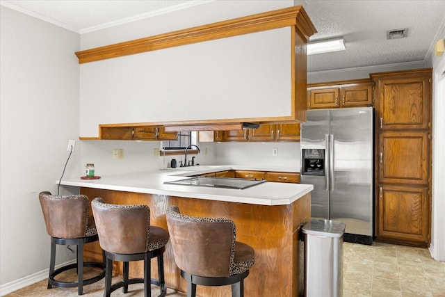 kitchen featuring stainless steel fridge, brown cabinetry, black electric stovetop, and light countertops