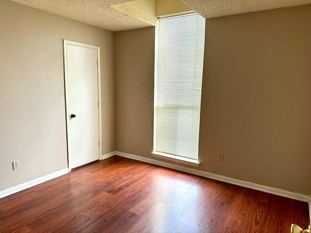 spare room featuring baseboards, wood finished floors, and a textured ceiling