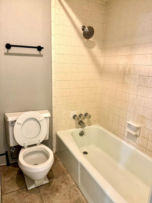 bathroom featuring toilet, tile patterned flooring, a textured wall, and shower / tub combination