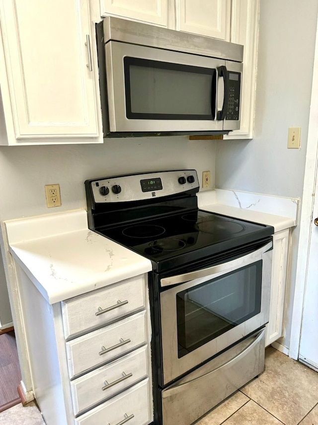 kitchen with appliances with stainless steel finishes, light tile patterned floors, and white cabinetry