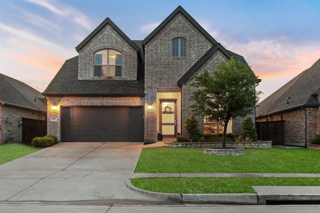 french provincial home with a lawn, driveway, brick siding, an attached garage, and fence
